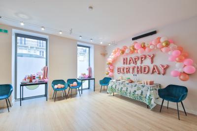 Salle décorée pour une fête avec ballons dorés, noirs et blancs, chiffre ’50’ en ballon et table avec boissons.