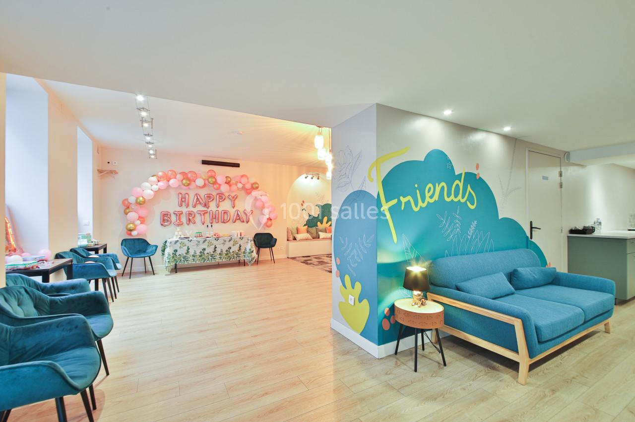 Salle lumineuse décorée pour un anniversaire, avec ballons, inscription ’Happy Birthday’ et coin salon coloré.