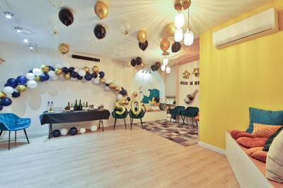 Salle décorée pour une fête avec ballons dorés, noirs et blancs, chiffre ’50’ en ballon et table avec boissons.