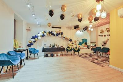 Salle décorée pour une fête avec ballons dorés, noirs et blancs, chiffre ’50’ en ballon et table avec boissons.