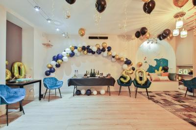 Salle décorée pour une fête avec ballons dorés, noirs et blancs, chiffre ’50’ en ballon et table avec boissons.