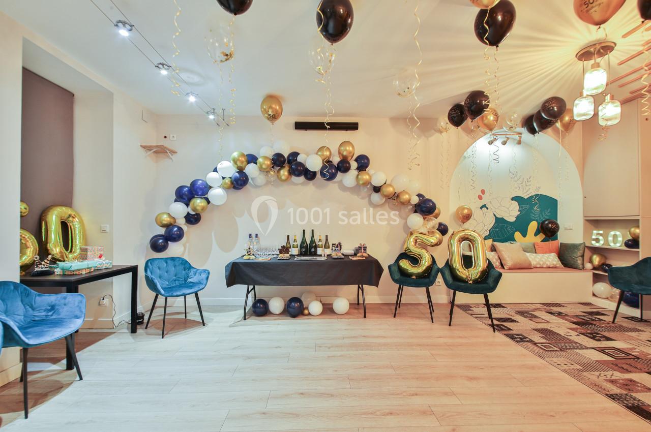 Salle décorée pour un anniversaire avec ballons dorés, noirs et blancs, table garnie et chiffre 50 en ballons.