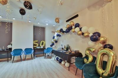 Salle décorée pour une fête avec ballons dorés, noirs et blancs, chiffre ’50’ en ballon et table avec boissons.