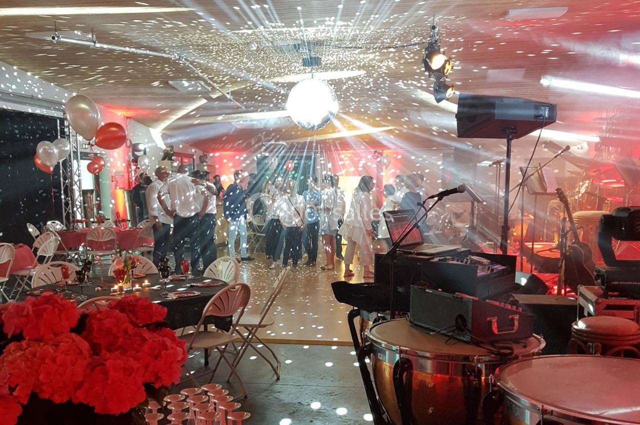 Salle décorée pour un événement festif avec piste de danse, éclairages colorés, tables dressées et instruments de musique.
