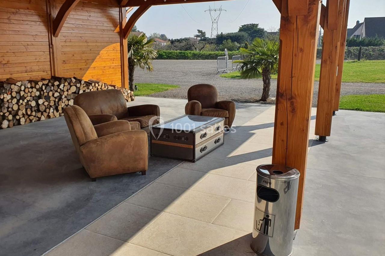 Salon extérieur avec fauteuils en cuir, table basse en métal et bois, sous une pergola en bois près d'un espace vert.