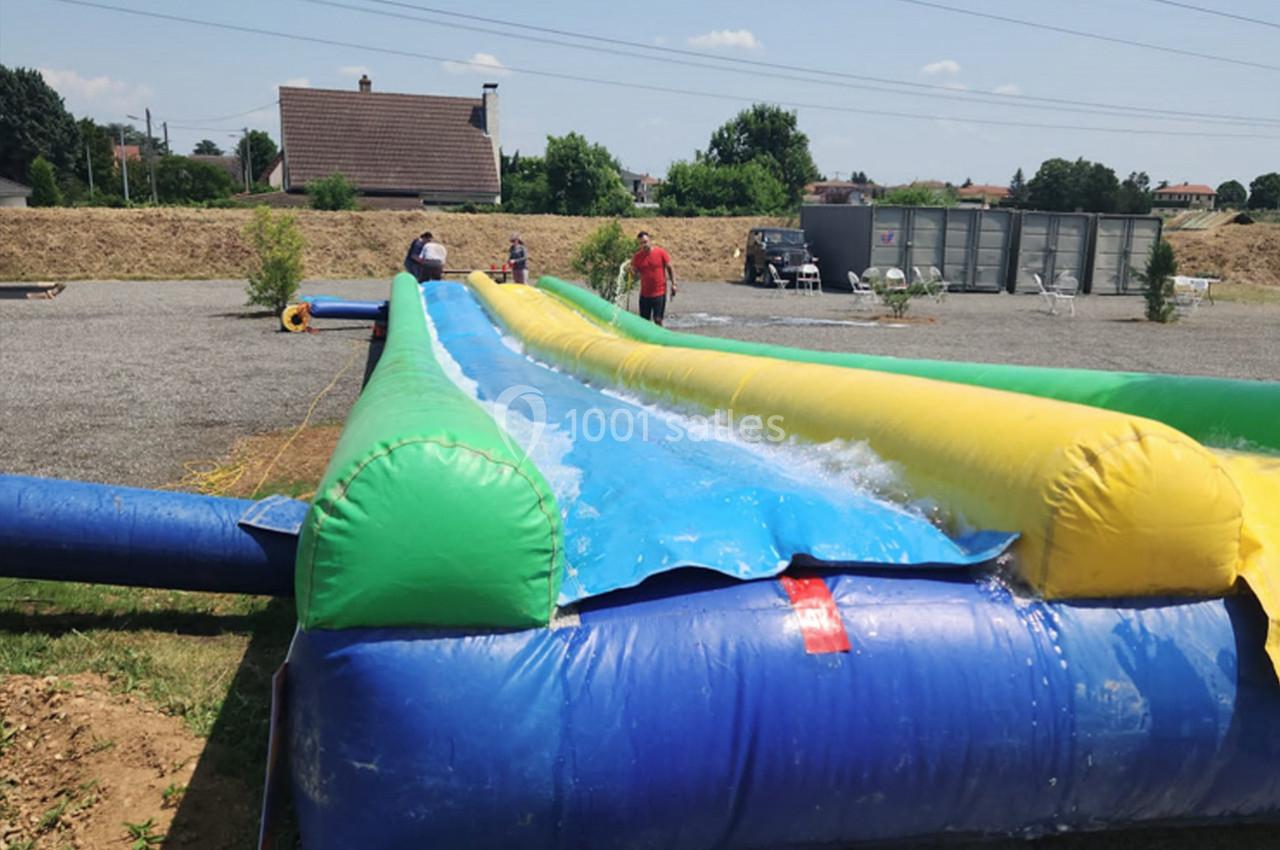 Structure gonflable colorée avec une piste d'eau, utilisée pour des activités de glisse en extérieur par temps ensoleillé.