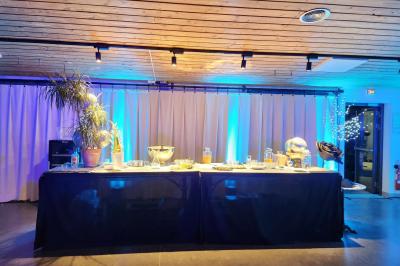 Espace intérieur en bois avec canapés, fauteuils, guirlande lumineuse et stand décoratif éclairé.