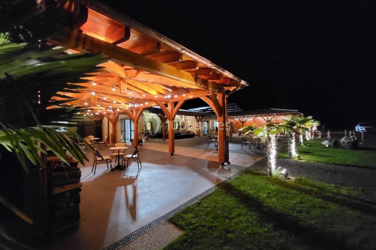 Terrasse en bois éclairée par des guirlandes lumineuses, entourée de palmiers et d'une pelouse, de nuit.