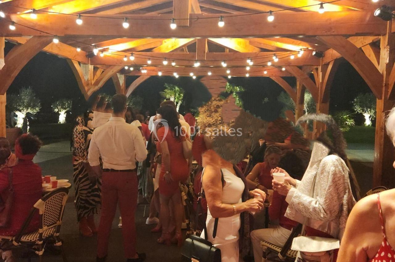 Groupe de personnes discutant sous une pergola en bois éclairée, lors d'un événement en soirée.