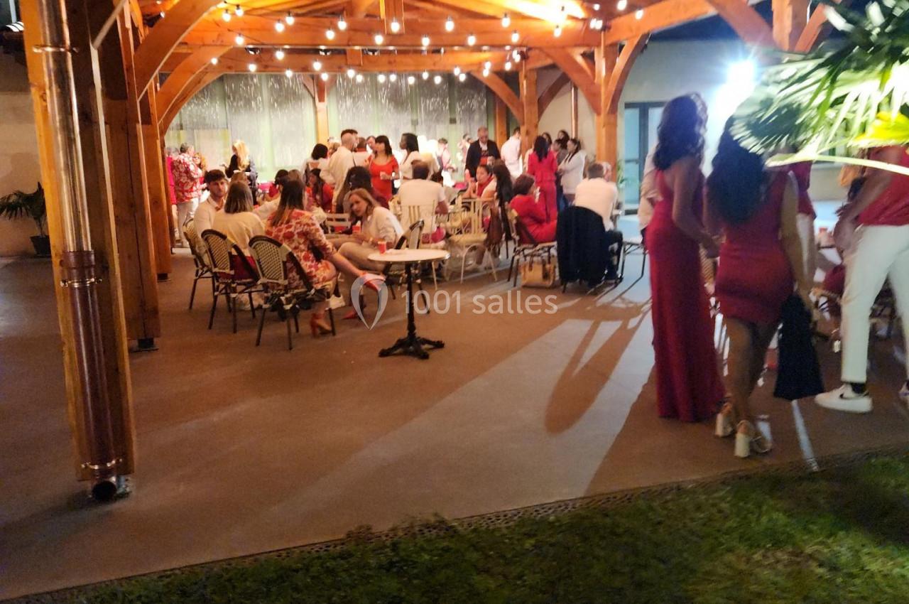 Groupe de personnes assises et debout sous une pergola en bois éclairée par des guirlandes lumineuses.