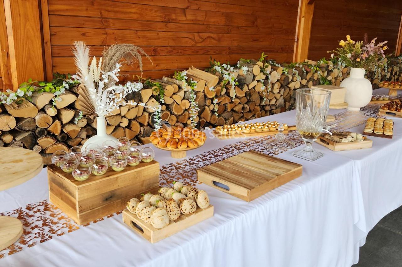 Table dressée avec nappes blanches, assortiments de desserts et décor rustique en bois et feuillages.