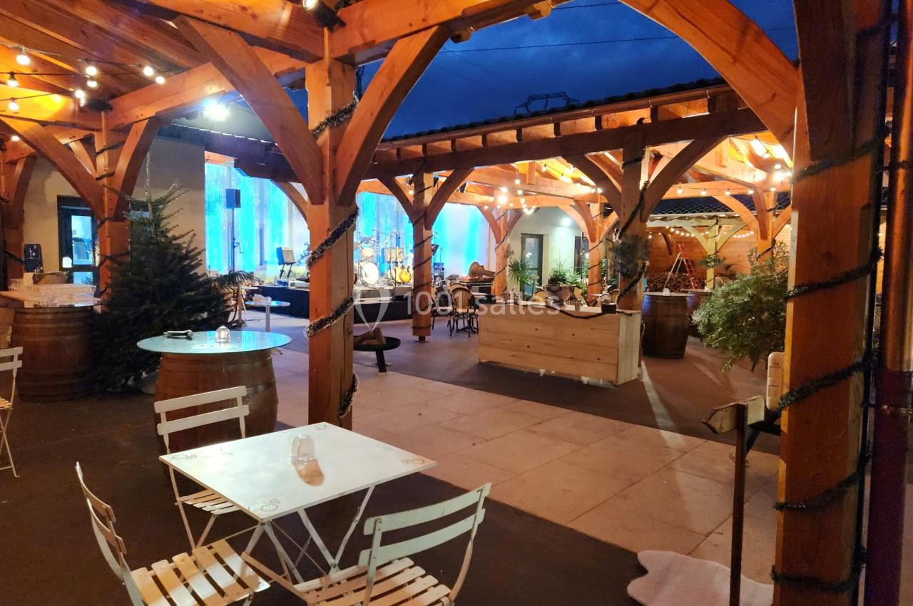 Terrasse couverte en bois avec tables blanches, guirlandes lumineuses et décorations, ambiance chaleureuse en soirée.