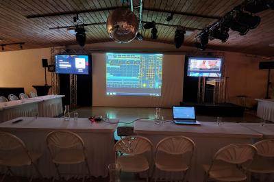 Espace intérieur en bois avec canapés, fauteuils, guirlande lumineuse et stand décoratif éclairé.