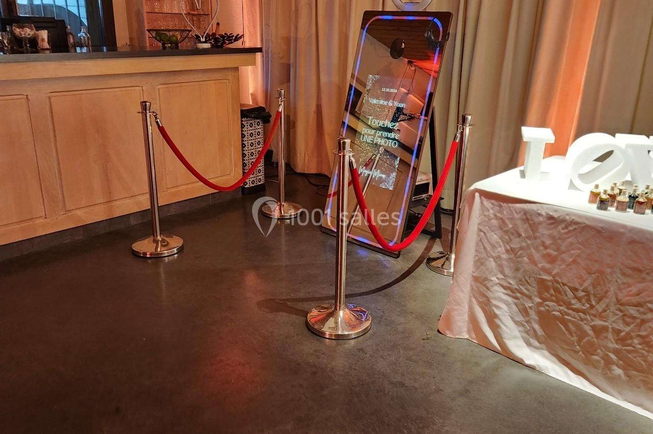 Un miroir interactif entouré de cordons rouges dans une salle avec un comptoir et des rideaux beiges.