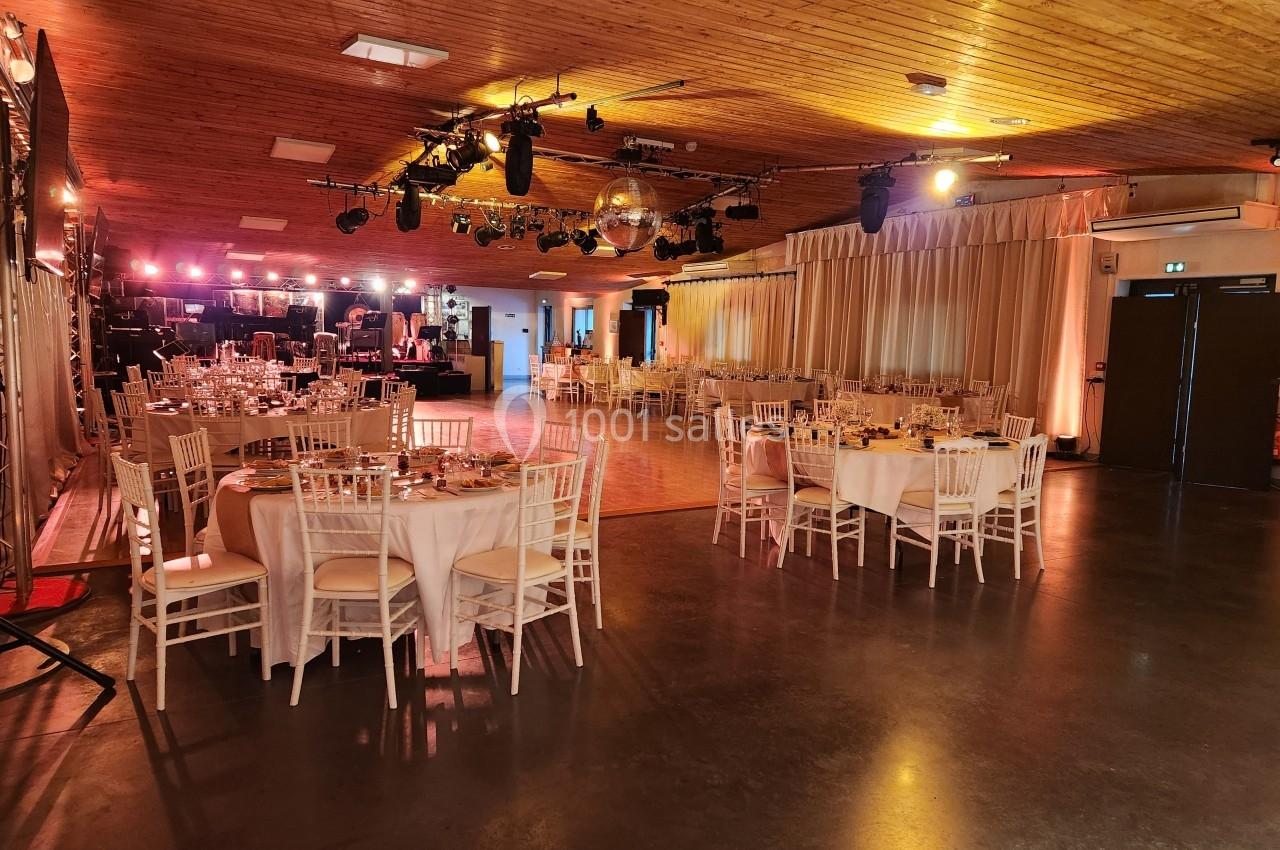 Salle de réception avec tables dressées, piste de danse centrale et éclairage chaleureux sous un plafond en bois.