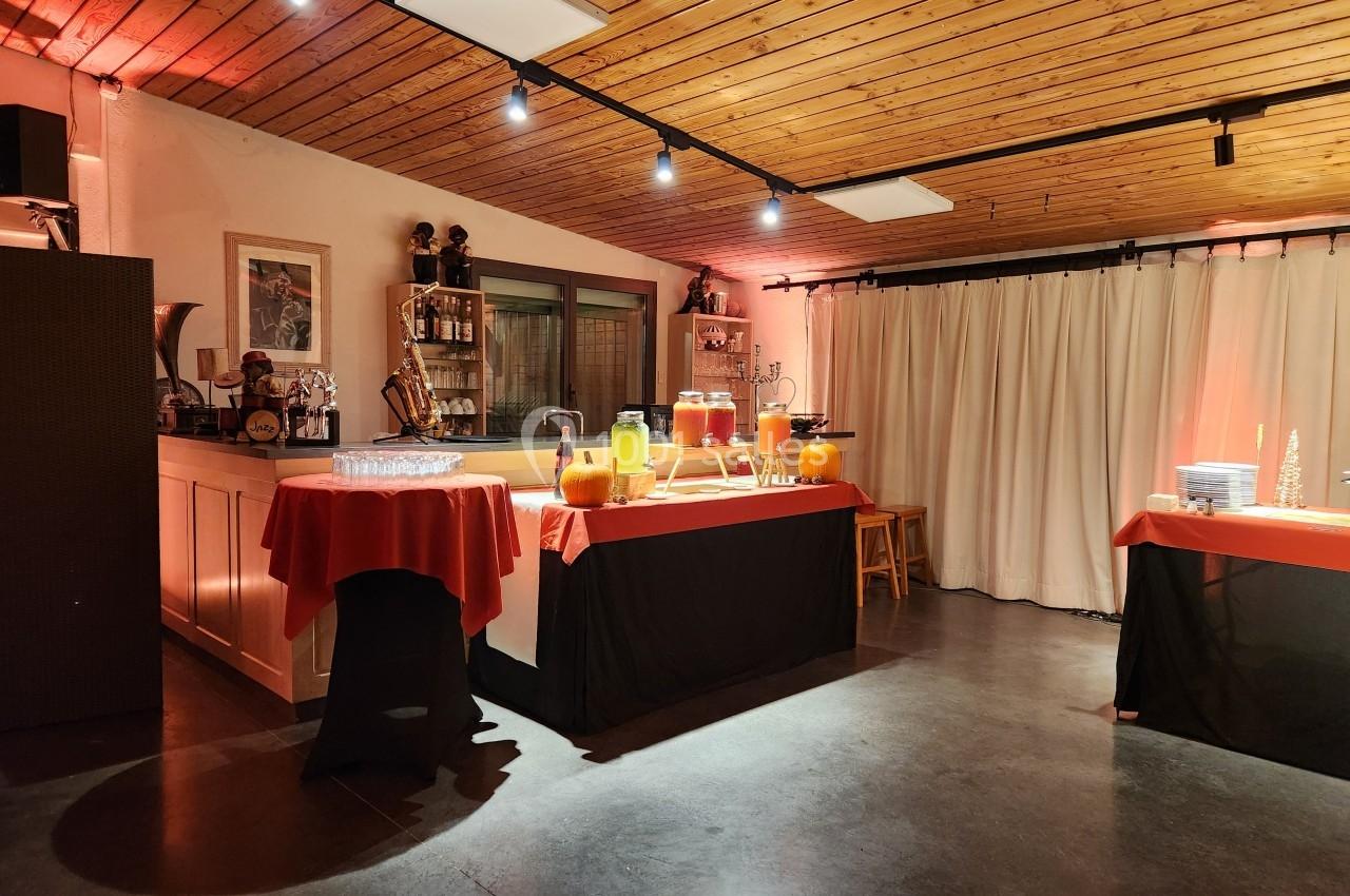 Salle décorée avec des tables couvertes de nappes rouges et noires, disposant de boissons et de citrouilles éclairées.