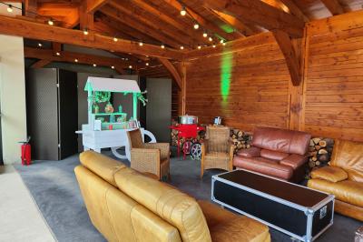 Espace intérieur en bois avec canapés, fauteuils, guirlande lumineuse et stand décoratif éclairé.