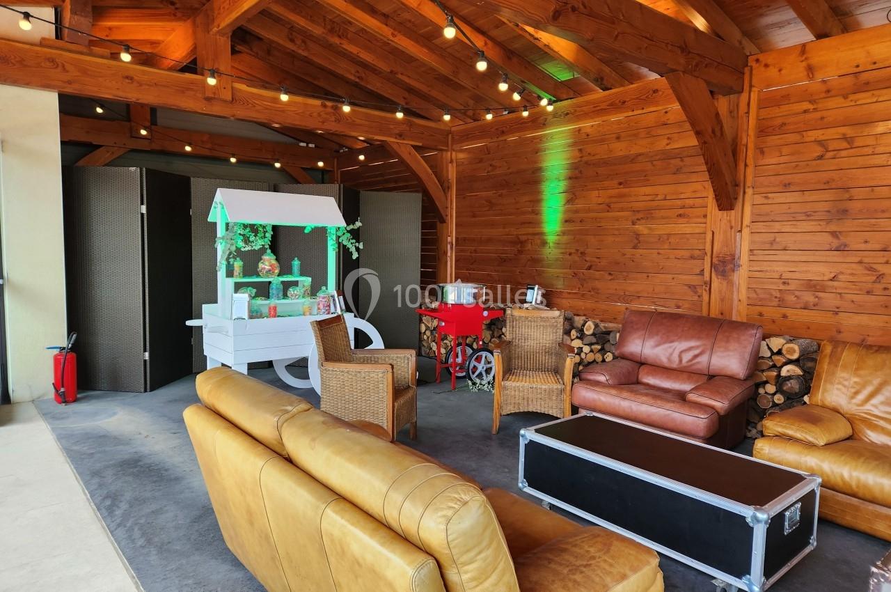 Espace intérieur en bois avec canapés, fauteuils, guirlande lumineuse et stand décoratif éclairé.