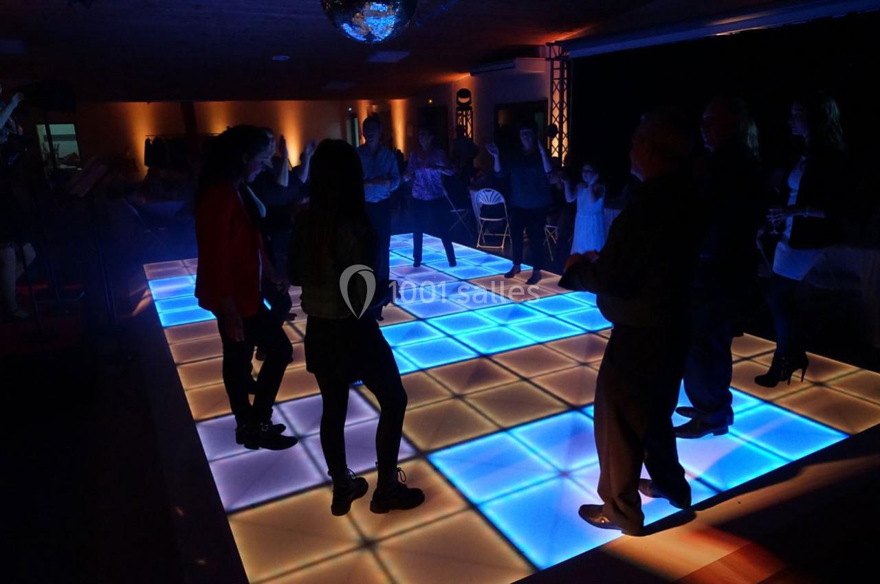 Personnes dansant sur une piste lumineuse à carreaux bleus et blancs dans une ambiance tamisée.