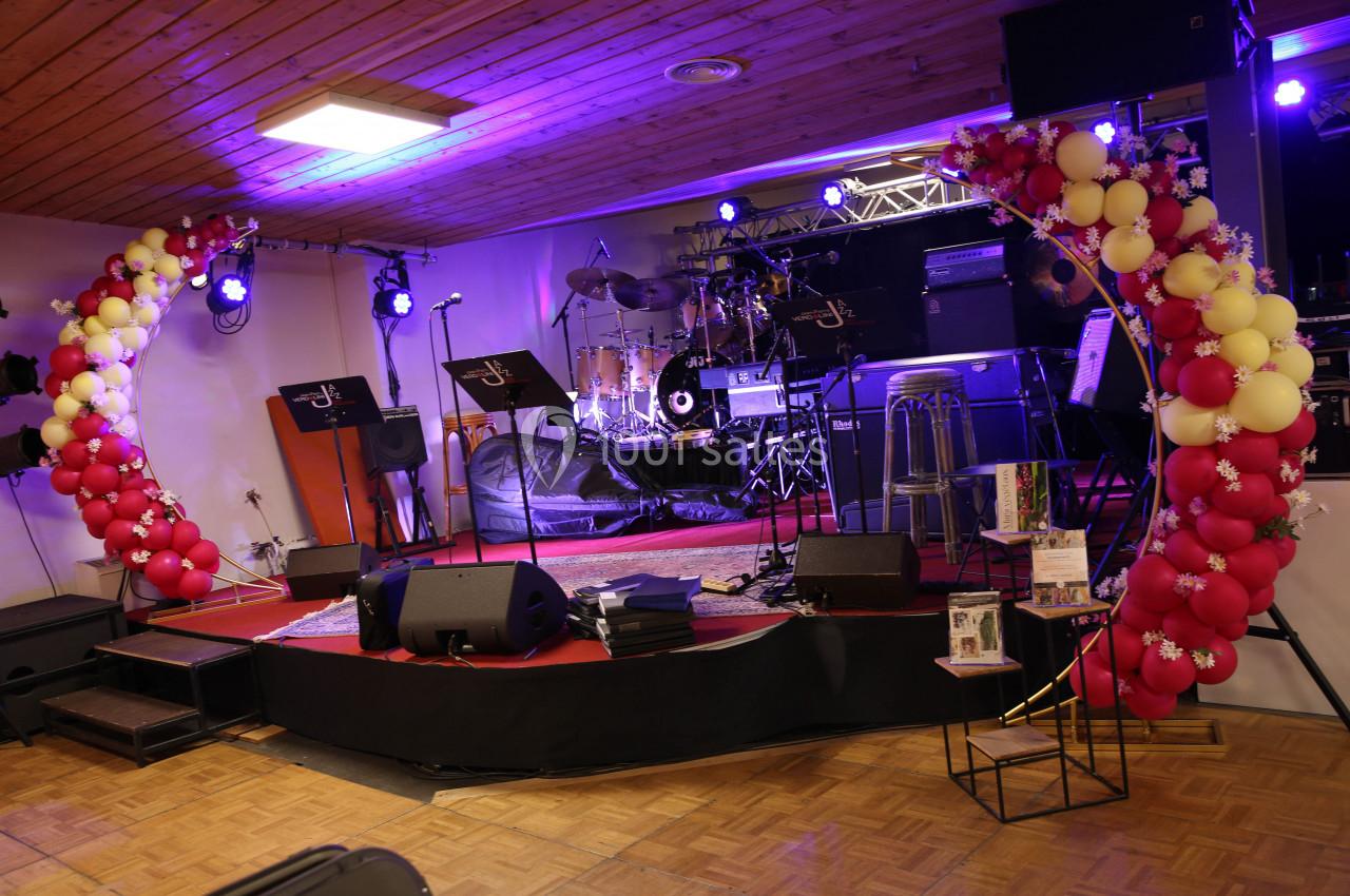 Scène décorée avec des ballons rouges et jaunes, équipée d'instruments de musique et de micros sous un éclairage violet.