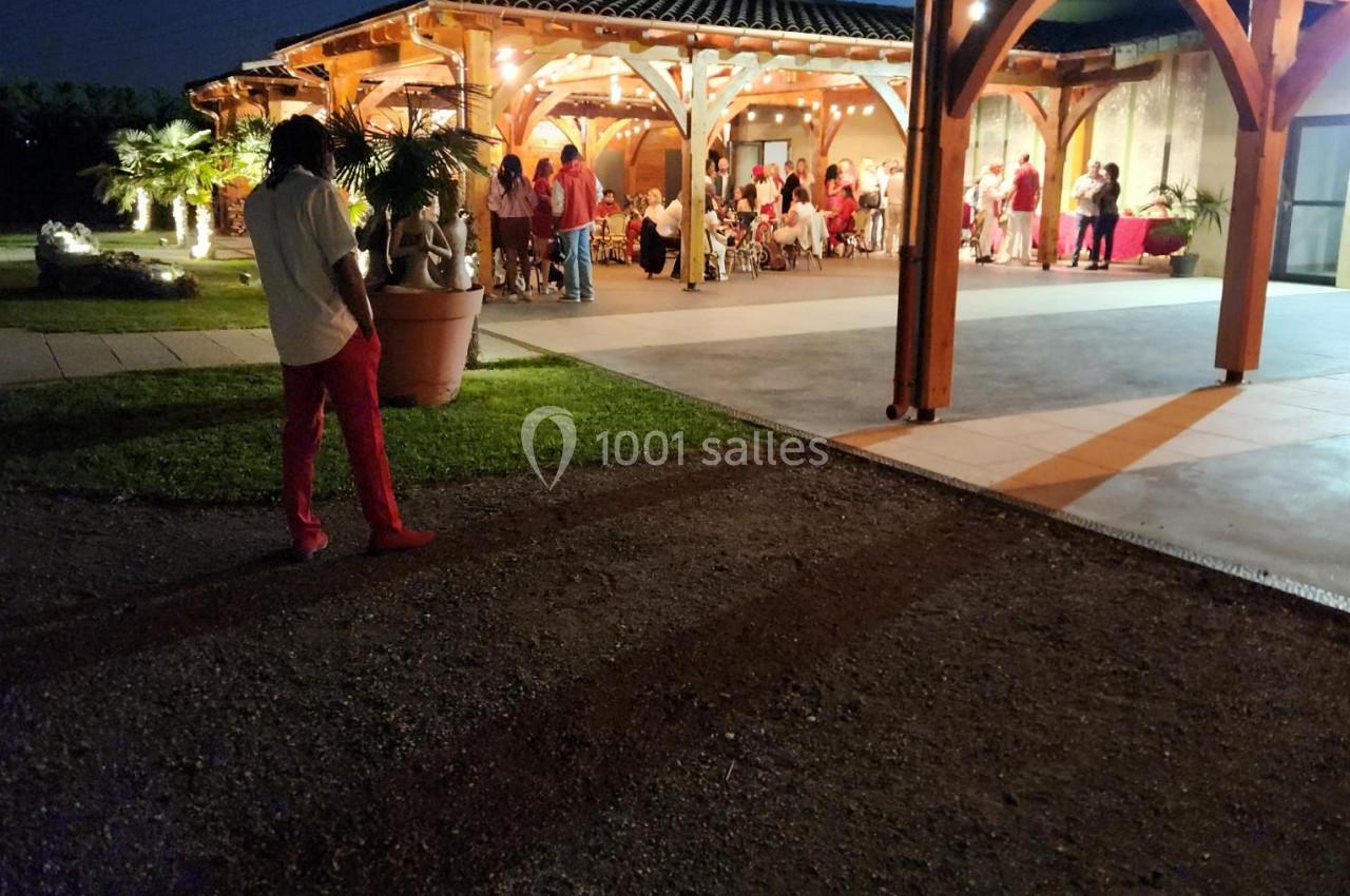 Groupe de personnes rassemblées sous une structure éclairée en soirée, avec un homme debout au premier plan.