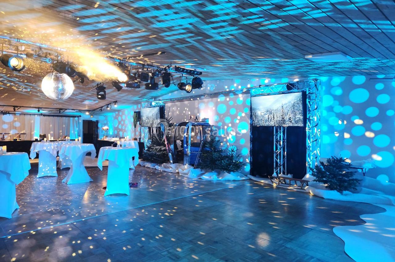 Salle décorée avec des lumières bleues, une boule disco, des tables hautes et des éléments évoquant un décor hivernal.