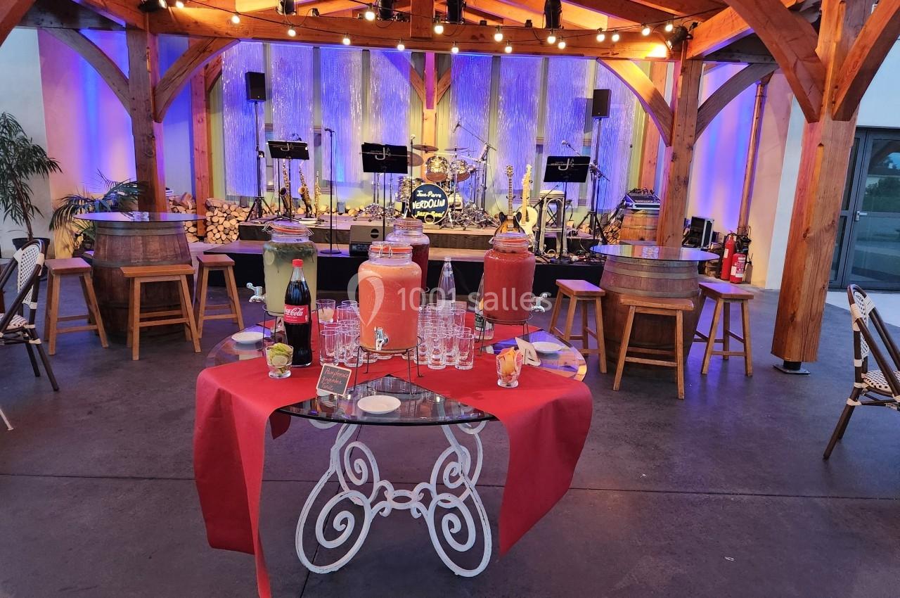 Buffet avec boissons et verres sur une table rouge, dans un espace couvert décoré avec éclairages et scène musicale en…