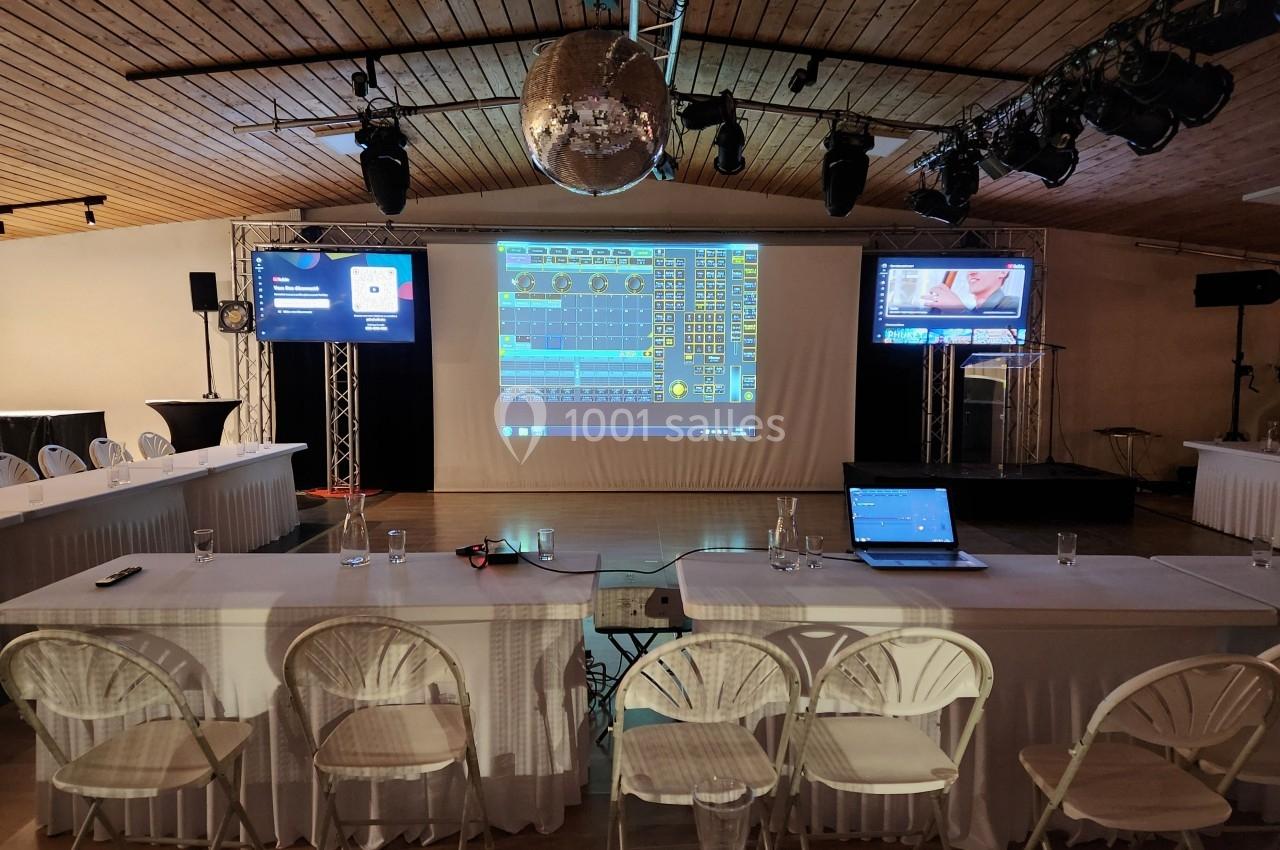 Salle de conférence équipée d'écrans, projecteurs et ordinateurs, avec des chaises alignées et une décoration moderne.