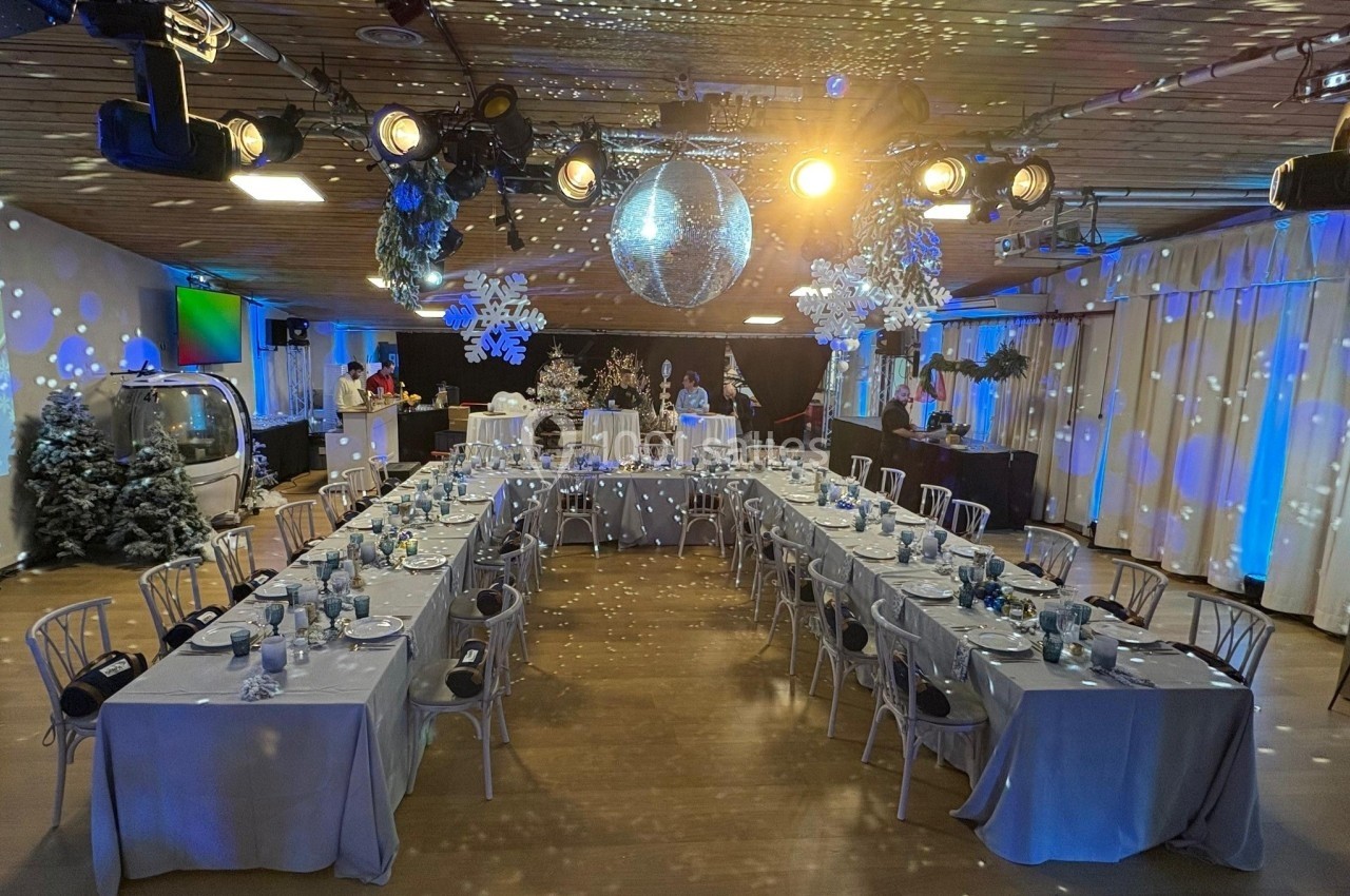 Salle décorée pour un événement festif avec tables dressées en U, éclairage tamisé et boule disco suspendue.