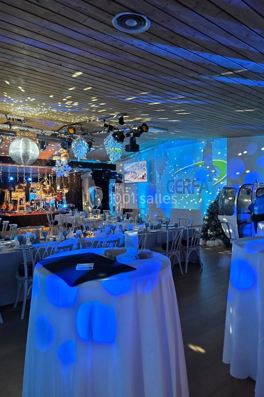 Salle décorée pour un événement, avec tables dressées, éclairages bleus, décorations hivernales et scène en arrière-plan.
