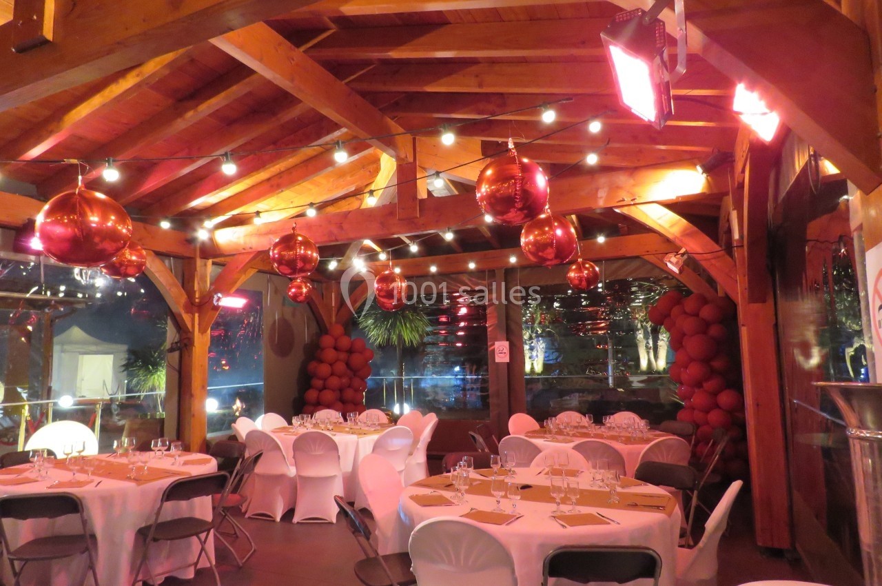 Salle décorée avec des guirlandes lumineuses, des suspensions rouges et des tables dressées pour un événement.