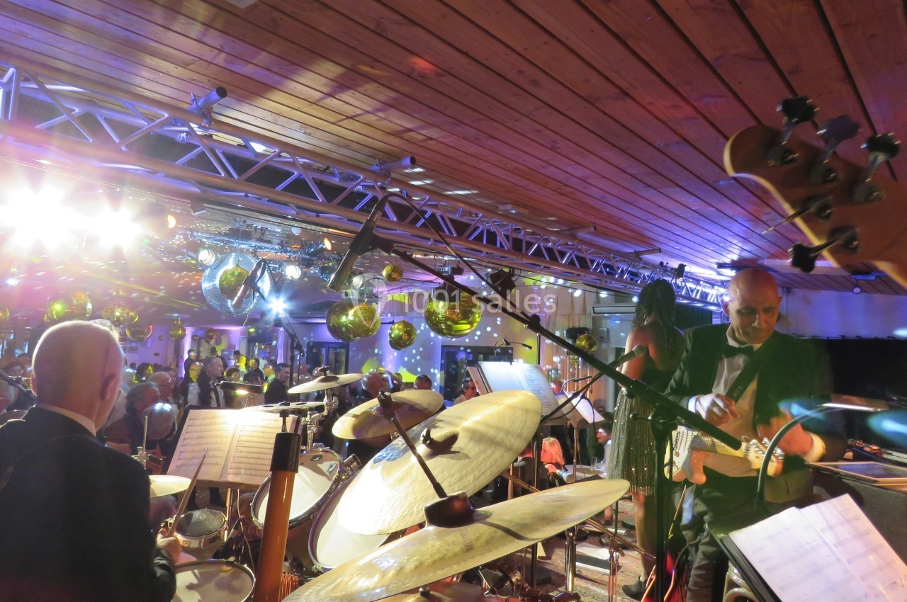 Musiciens jouant sur scène dans une salle éclairée, avec des instruments et des décorations suspendues visibles.