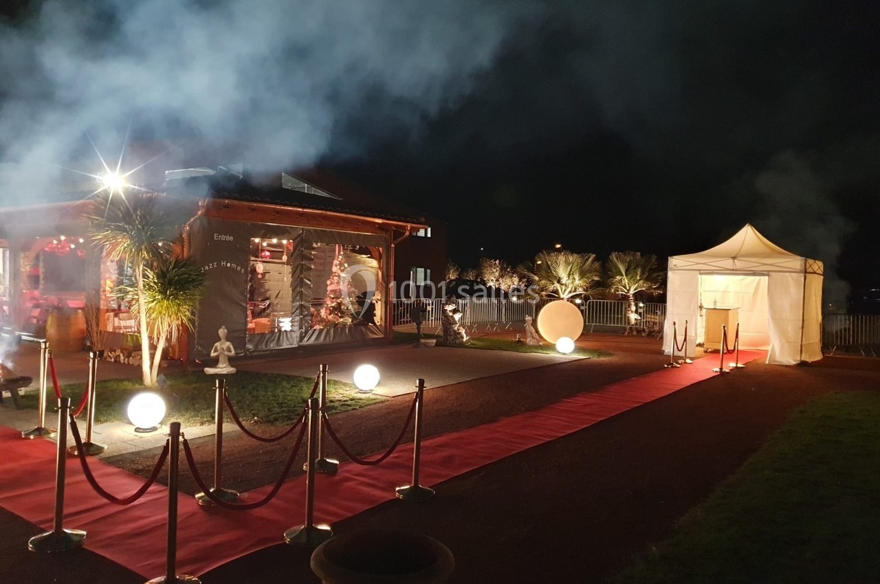 Entrée d'un événement nocturne avec tapis rouge, lampes sphériques, tente blanche et bâtiment éclairé en arrière-plan.