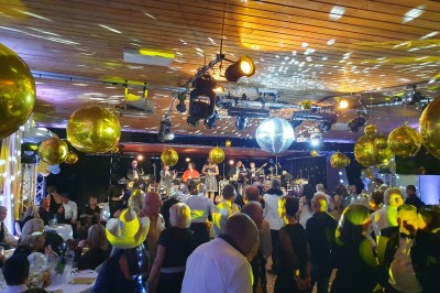 Un groupe de musiciens et chanteurs joue sur une scène éclairée dans une salle avec un public assis.