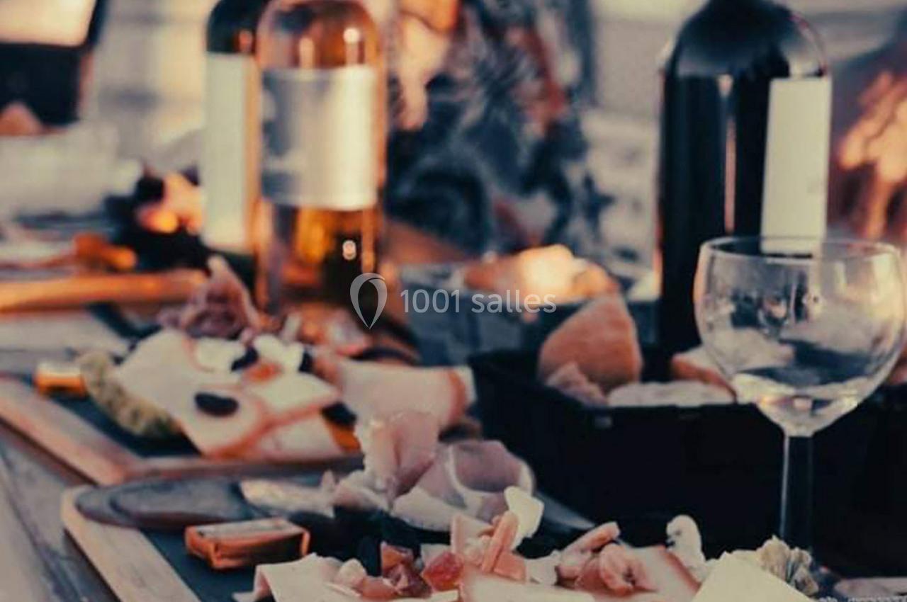 Plateau de charcuterie et fromages sur une table avec des bouteilles de vin et des verres en arrière-plan.