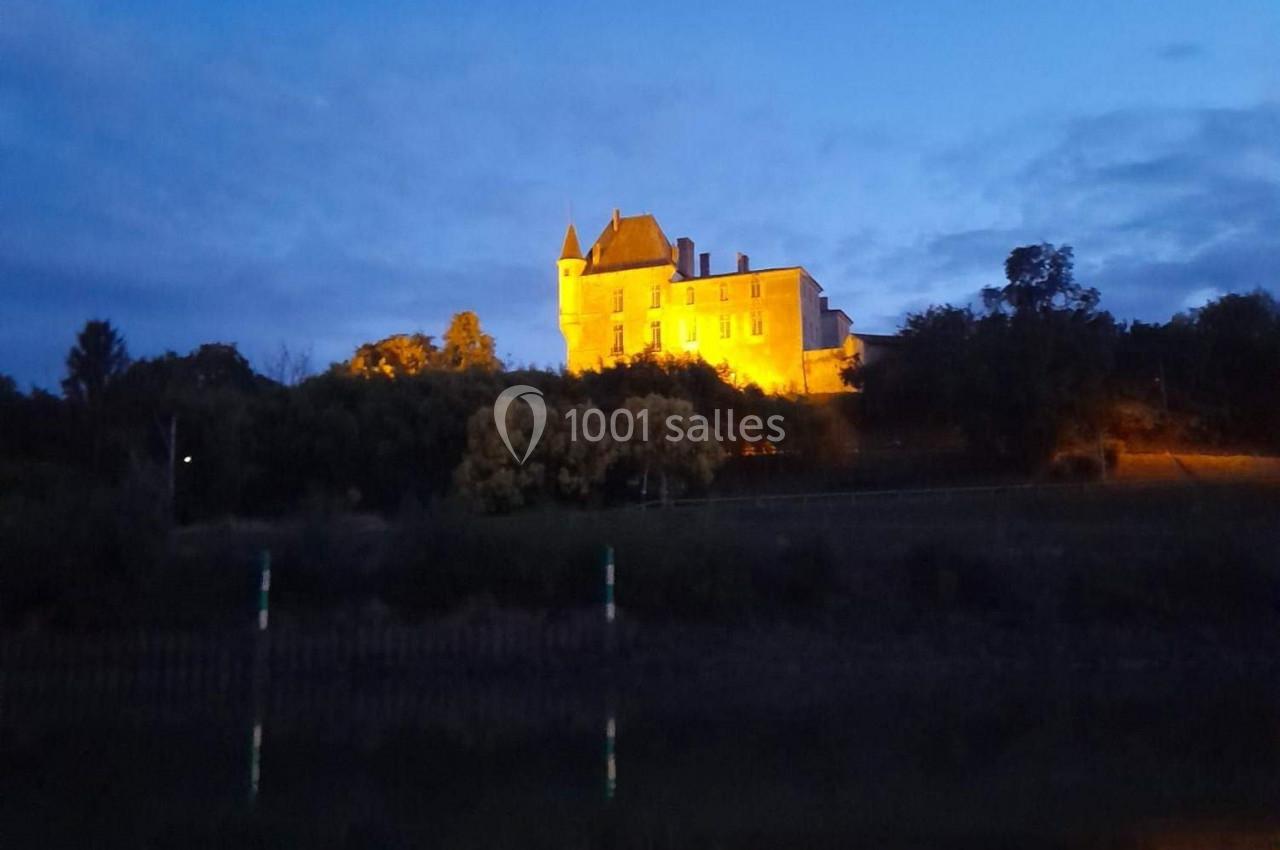 Château illuminé au sommet d'une colline, reflété dans l'eau calme au crépuscule.