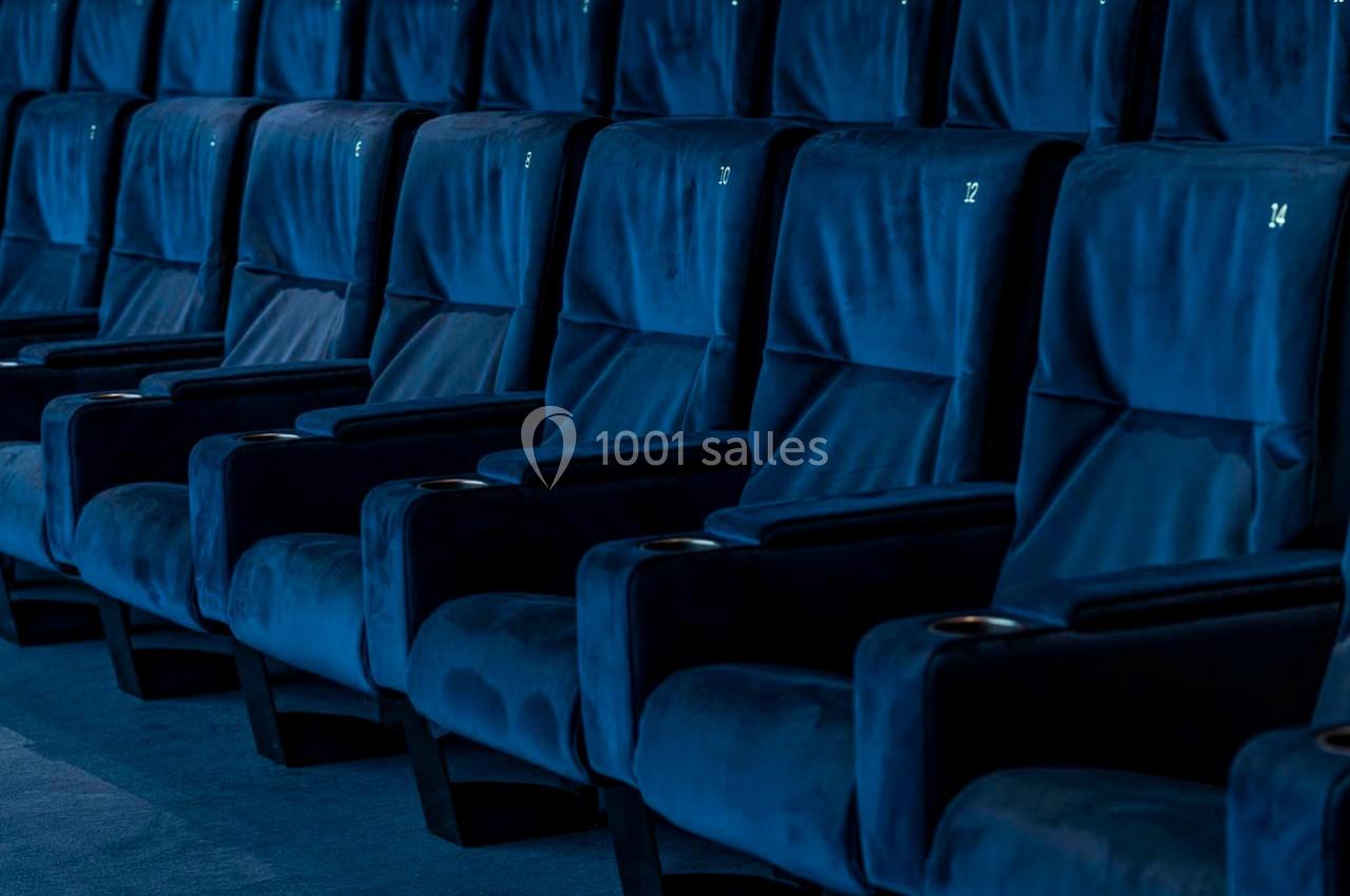 Rangée de fauteuils bleus numérotés dans une salle de cinéma vide.