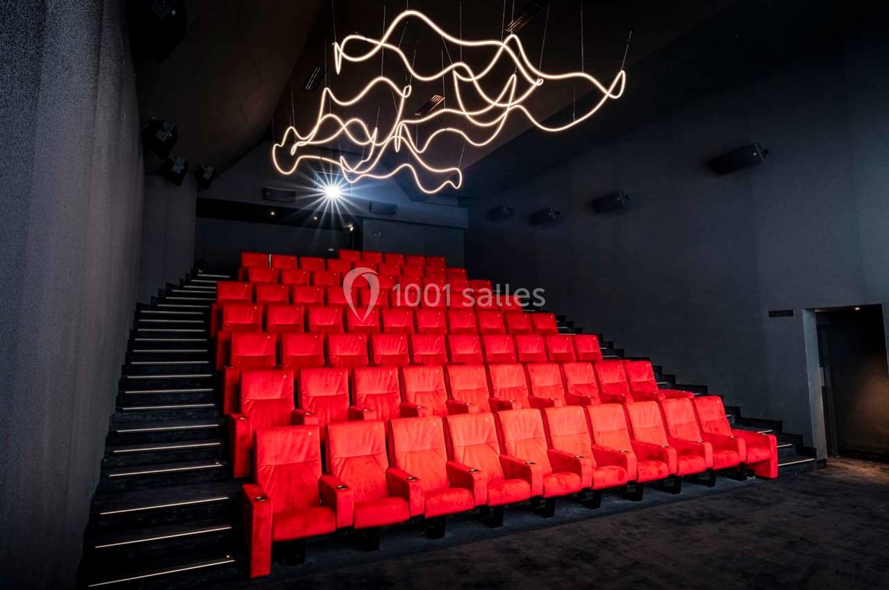 Salle de cinéma moderne avec sièges rouges alignés en gradins et éclairage design suspendu au plafond.