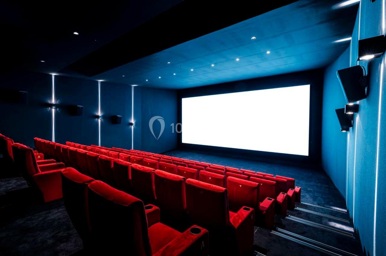 Salle de cinéma vide avec des rangées de sièges rouges et un grand écran blanc allumé.