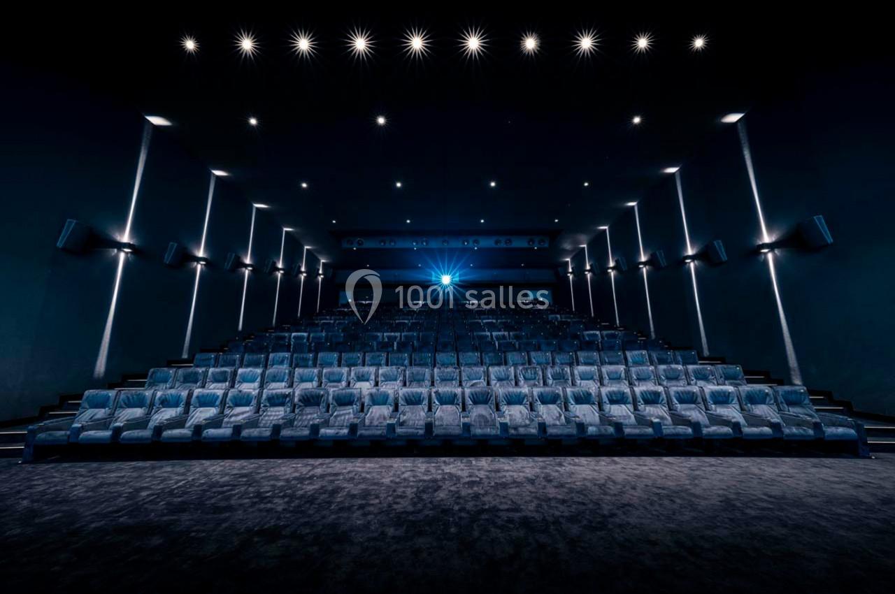 Salle de cinéma vide avec rangées de sièges alignés et éclairage tamisé, vue depuis l'écran.