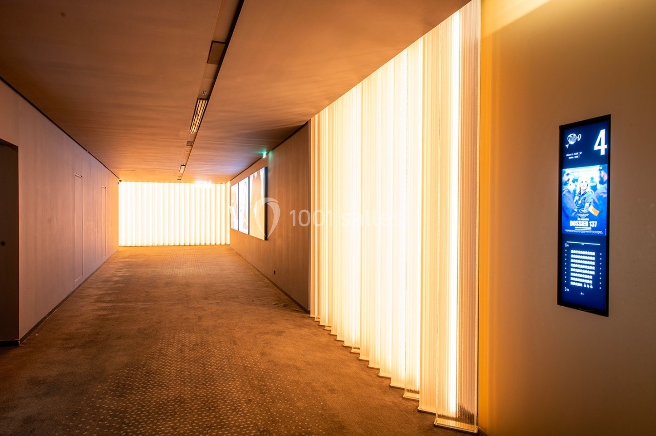 Couloir moderne avec éclairage mural lumineux et écran numérique affichant des informations sur la droite.