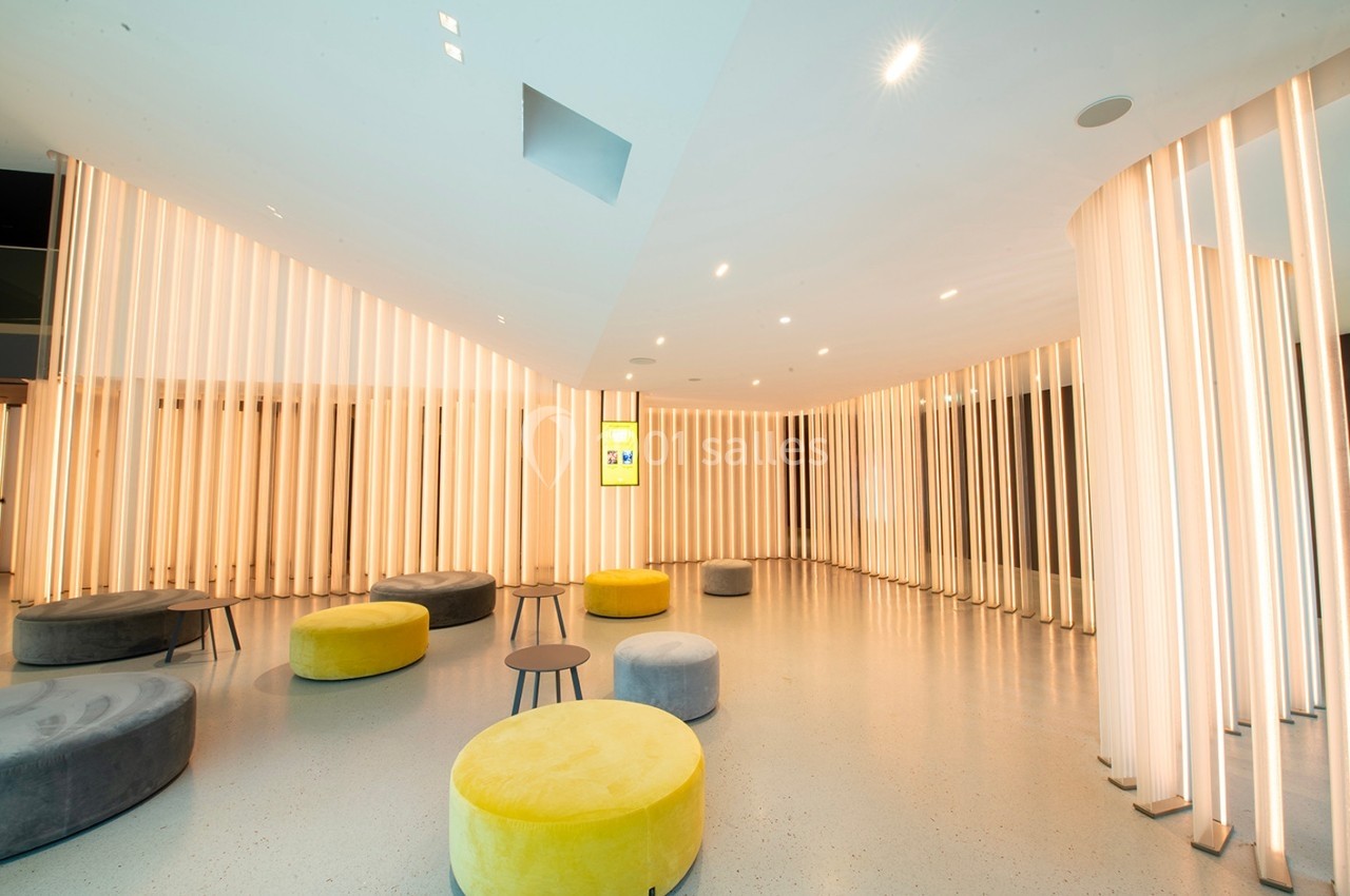 Salle moderne avec murs lumineux en colonnes verticales, poufs ronds jaunes et gris, et tables basses.