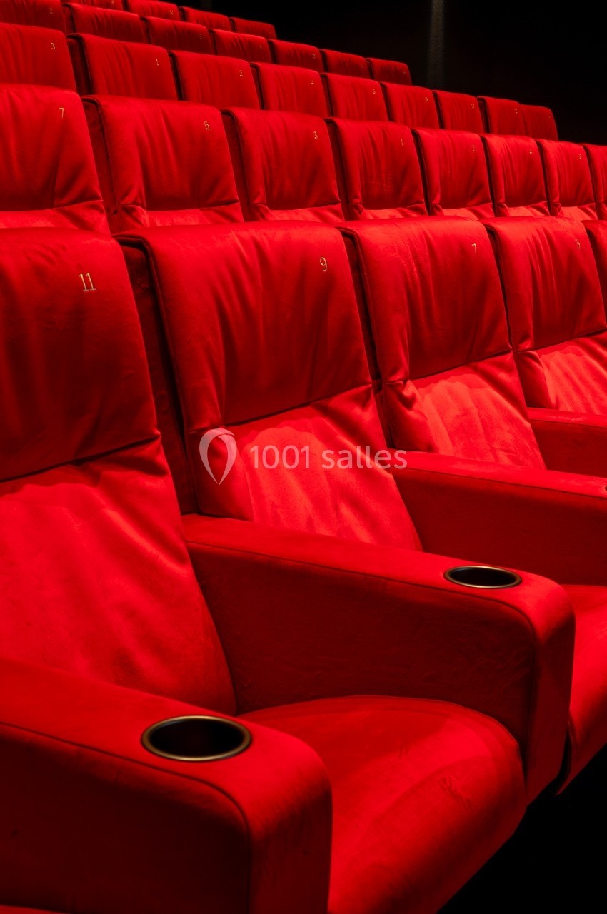 Rangée de fauteuils rouges numérotés dans une salle de cinéma, avec porte-gobelets intégrés.