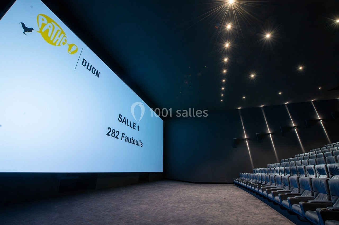 Salle de cinéma moderne avec écran géant, rangées de fauteuils bleus et éclairage tamisé au plafond.