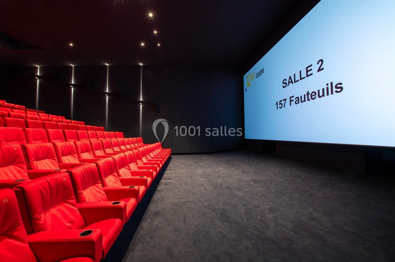 Salle de cinéma moderne avec des sièges rouges alignés et un écran affichant ’Salle 2, 157 fauteuils’.