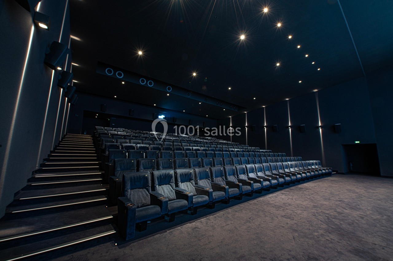 Salle de cinéma vide avec des rangées de sièges en velours bleu et un éclairage tamisé.