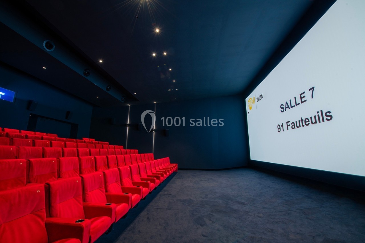 Salle de cinéma vide avec des fauteuils rouges, un écran affichant ’Salle 7, 91 fauteuils’ et un éclairage tamisé.