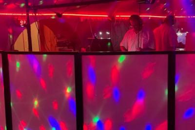 Un DJ mixe derrière une table éclairée par des lumières colorées dans une ambiance de soirée festive.