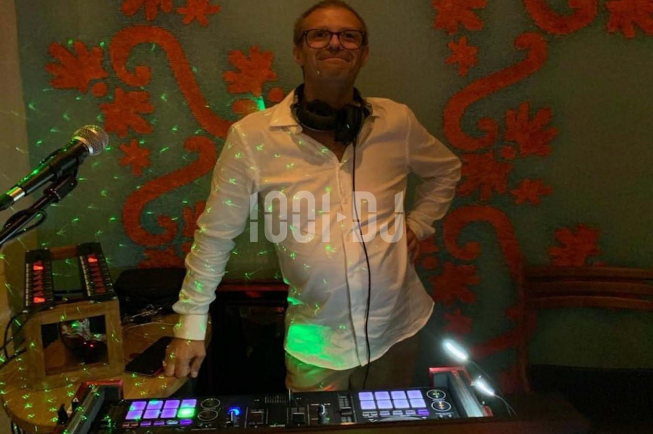 Homme debout derrière une table de mixage éclairée, portant un casque audio, avec un fond décoratif et des lumières colorées.