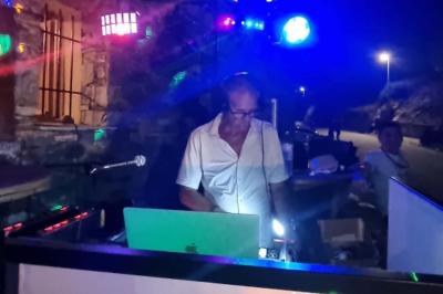 Un DJ mixe derrière une table éclairée par des lumières colorées dans une ambiance de soirée festive.